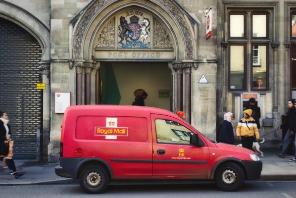 A red Royal Mail van parked in the street outside a post office