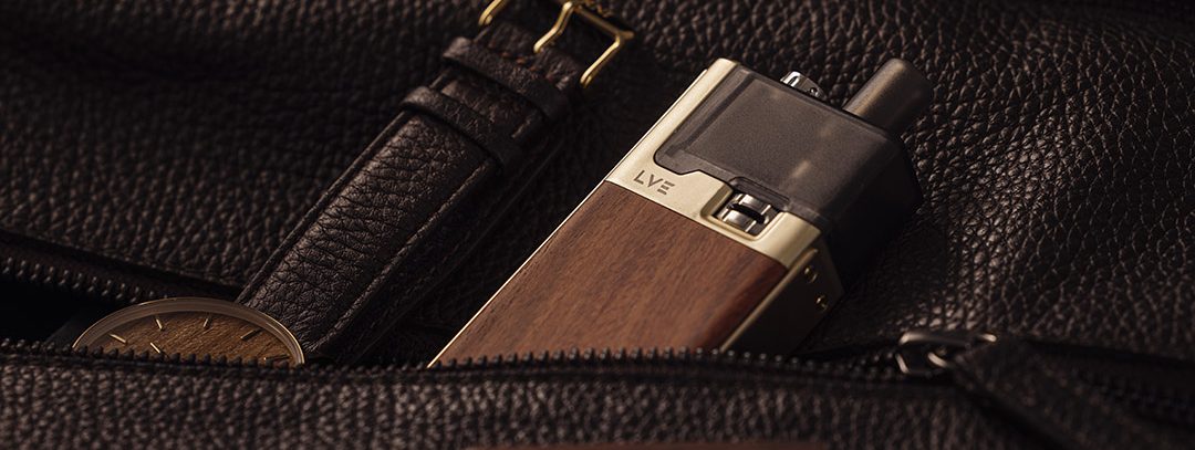 Gold orion ii with wooden panels, poking out of a leather handbag zipped pocket next to a leather strapped analogue watch