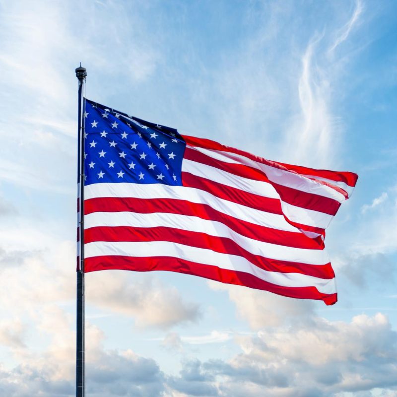 Flag of United States of America being waved in the breeze against blue sky